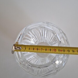 May include: A clear, round crystal bowl with a textured, swirling design. A yellow tape measure is placed across the bowl, showing a diameter of approximately 4.5 inches. The bowl is on a white background.
