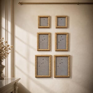 May include: Six gold-coloured picture frames are mounted on a beige wall. The frames are arranged in two rows, with two square frames at the top and four rectangular frames below. Each frame has a grey backing and small black pins.