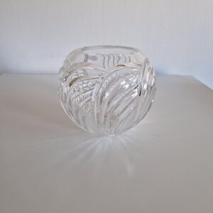 May include: A clear, spherical glass vase with a textured, leaf-like pattern. The vase is designed with a wide opening and sits on a white surface. The glass reflects light, creating shadows.