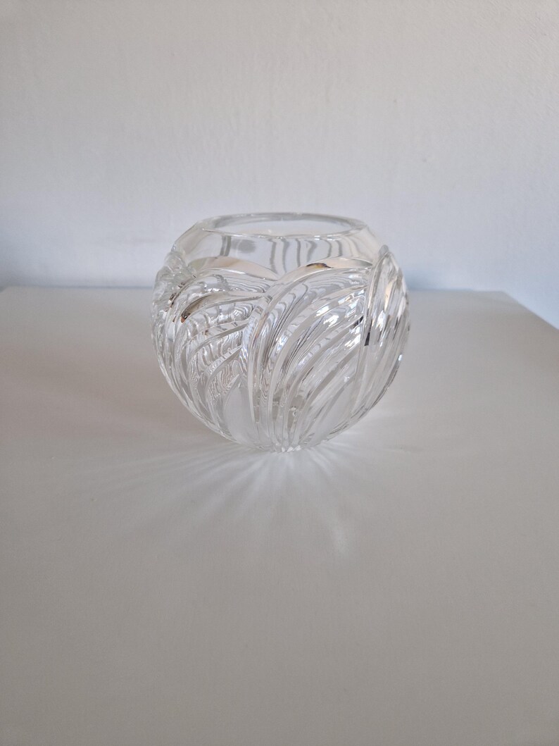 May include: A clear, spherical glass vase with a textured, leaf-like pattern. The vase is designed with a wide opening and sits on a white surface. The glass reflects light, creating shadows.
