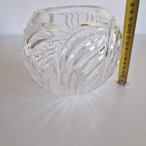 May include: A clear, round glass vase with a textured, swirling design. The vase is approximately 5 inches in diameter. The vase is sitting on a white surface.