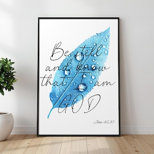 以下が含まれることがあります： 水滴が付いた青い葉が描かれた、額入りのアートプリント。 「Be still and know that I am GOD」というテキストが筆記体で書かれており、聖書のジョン46:10の引用が含まれています。