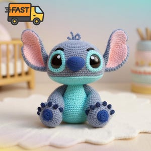 Puede incluir: Mu&ntilde;eco Stitch hecho a mano con ganchillo, con cuerpo azul y gris, ojos negros grandes, nariz azul y orejas grandes forradas en rosa. El mu&ntilde;eco tiene patas azules y est&aacute; sentado sobre una superficie blanca. La imagen incluye un icono de cami&oacute;n de reparto.