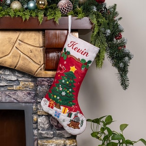 May include: A red Christmas stocking featuring the embroidered name Kevin at the top. The stocking displays a green Christmas tree, colorful gift boxes, a small gray rabbit, and holly leaves. It is made of fabric and includes a white hanging loop.