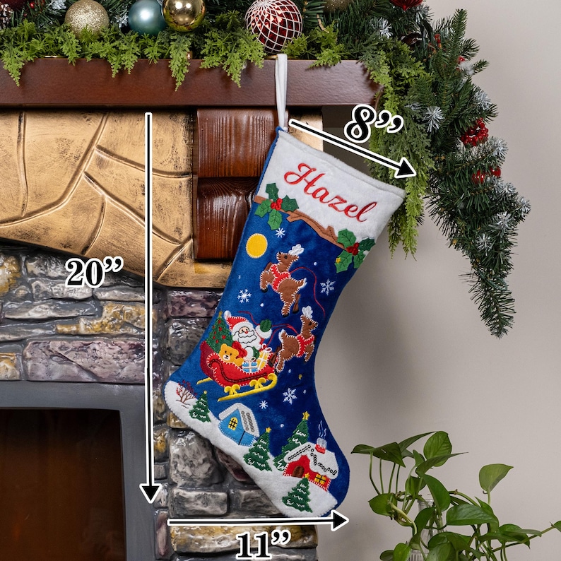 May include: A blue Christmas stocking with a white cuff embroidered with the name Hazel. The stocking features a festive scene with Santa in a sleigh, reindeer, a yellow moon, and snowy houses. It measures 20 inches in height, 8 inches at the top, and 11 inches at the base.