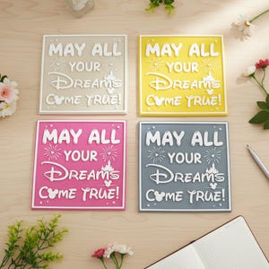 May include: Four square decorative signs with the text "MAY ALL YOUR DREAMS COME TRUE!" in white. The signs are in beige, yellow, pink, and gray. Each sign features a castle and Mickey Mouse ears.
