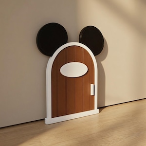 May include: A brown decorative door with a white frame and oval accent, designed with black Mickey Mouse ears. The door is set against a neutral wall and floor, creating a whimsical accent piece.
