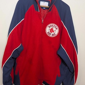 Op de afbeelding: Een rood en marineblauw jack met ritssluiting en het Boston Red Sox-logo op de borst. Het jack heeft lange mouwen met witte biezen, een geribbelde kraag en een rode voering. Een label in de nek bevat de tekst Genuine Merchandise.