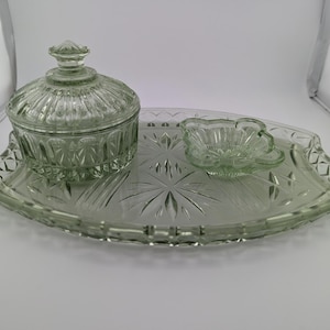 May include: A vintage green glass serving set. The set includes a covered dish, a small flower-shaped dish, and a decorative tray. The glass has a textured, cut-glass design. The tray is approximately 12 inches long.