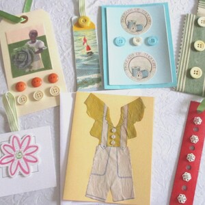 May include: A collection of handmade tags and cards. The tags feature images of a person with a cabbage, a sailboat, and a yellow jumpsuit. The cards have flower and text designs. Embellished with buttons and ribbons.