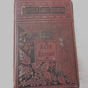 May include: A vintage hardcover book titled American Family Robinson, Alta Edition. The cover is a deep reddish-brown with embossed floral and leaf patterns. The title and edition are printed in dark rectangular frames on the front cover.