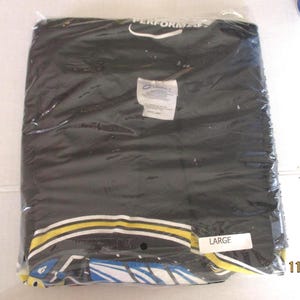 May include: A black t-shirt sealed in a clear plastic bag. The shirt features a design with yellow, white, and blue details. A label marked "LARGE" is affixed to the packaging.