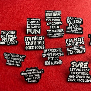 Peut inclure: Plusieurs épingles émaillées noires et blanches avec des phrases humoristiques sur un fond rouge. Les épingles présentent des citations telles que "I'm sorry did I roll my eyes out loud?" et "I'm not arguing, I'm just explaining why I'm right."