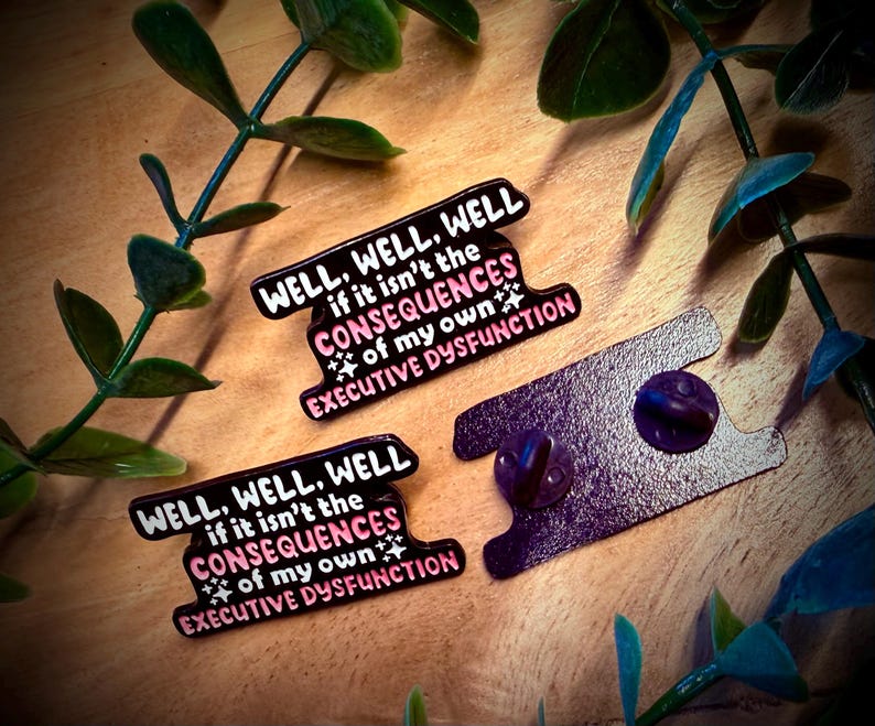 Puede incluir: Tres pines de esmalte con el texto "WELL, WELL, WELL if it isn't the CONSEQUENCES of my own EXECUTIVE DYSFUNCTION" en blanco y rosa sobre fondo negro. Los pines est&aacute;n sobre una superficie de madera con hojas verdes.