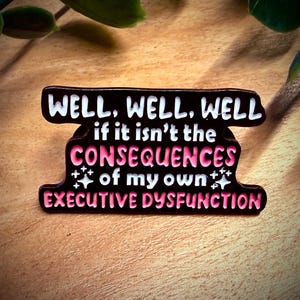 Könnte beinhalten: Ein schwarzer und rosa Emaille-Pin mit dem Text "WELL, WELL, WELL if it isn't the CONSEQUENCES of my own EXECUTIVE DYSFUNCTION". Der Pin hat einen weißen Rand und Sternakzente.