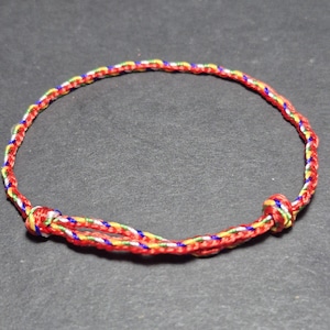 Può includere: Un braccialetto fatto a mano con un design intrecciato. Il braccialetto presenta un vivace mix di fili rossi, gialli, verdi e blu. Le estremità sono annodate insieme per formare una chiusura sicura. Un accessorio semplice e colorato.