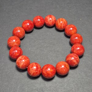 May include: A red coral bead bracelet. The bracelet features round, polished beads in varying shades of red and orange. The beads are strung together to form a circular shape, suitable for wrist wear. The coral beads have natural patterns.