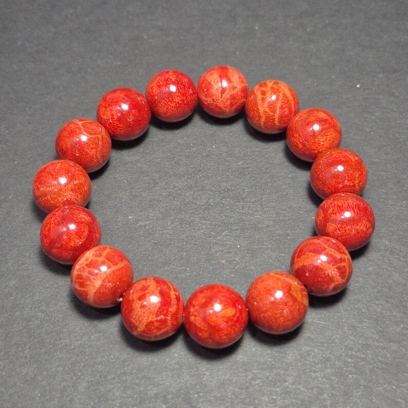 May include: A red coral bead bracelet. The bracelet features round, polished beads in varying shades of red and orange. The beads are strung together to form a circular shape, suitable for wrist wear. The coral beads have natural patterns.