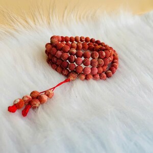 Puede incluir: Una pulsera de varias capas compuesta por peque&ntilde;as cuentas rojas redondas y texturizadas. La pulsera presenta un cord&oacute;n rojo fino que se extiende desde el bucle principal, terminando en un peque&ntilde;o grupo de cuentas rojas a juego como borla.