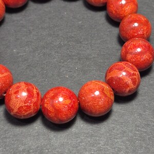 May include: Close-up of a bracelet featuring round, vibrant red beads. The beads have a textured surface with darker red patterns. The bracelet is strung together, showcasing the natural color and design of the beads.