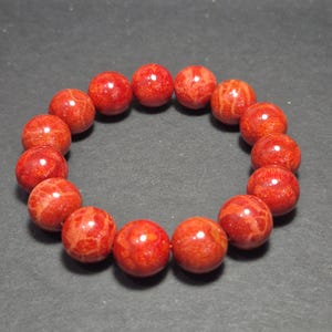 Peut inclure: Un bracelet de perles en corail rouge. Le bracelet présente des perles rondes et polies avec des motifs naturels. Les perles sont enfilées ensemble, formant une forme circulaire. Les perles de corail sont d'un rouge vif.