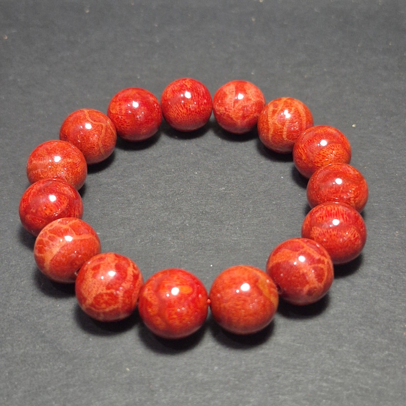 May include: A red coral bead bracelet. The bracelet features round, polished beads with natural patterns. The beads are strung together, forming a circular shape. The coral beads have a vibrant red color.