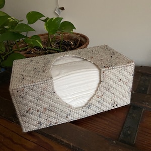 May include: A white tissue box cover with a speckled pattern in shades of brown, gray, and black. The cover is made of a woven fabric and has a rectangular shape.