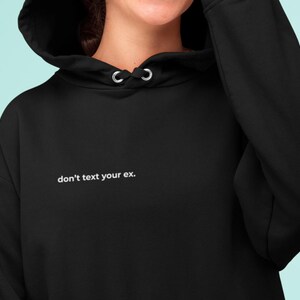 Könnte beinhalten: Schwarzer Kapuzenpullover mit Kordelzug und dem weißen Text "don't text your ex.". Der Hoodie besteht aus einem weichen Material und hat eine lockere Passform. Das Bild zeigt eine Nahaufnahme des Oberkörpers.