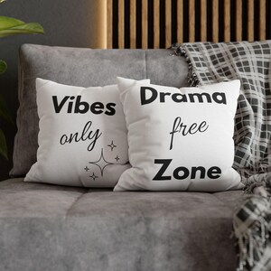 Könnte beinhalten: Zwei weiße Kissen mit schwarzem Text. Auf einem Kissen steht "Vibes only" mit Sternen-Grafiken. Auf dem anderen Kissen steht "Drama free Zone". Die Kissen liegen auf einem grauen Sofa mit einer gemusterten Decke im Hintergrund.
