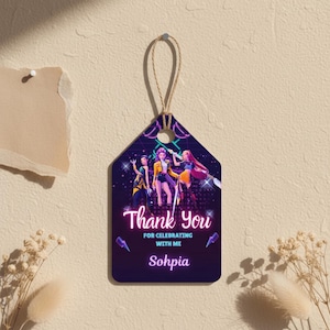 May include: A hanging tag with a string, featuring a graphic of three women in vibrant outfits. The tag displays the words "Thank You" and "For Celebrating With Me" in a neon font, with the name "Sohpia" below the text.