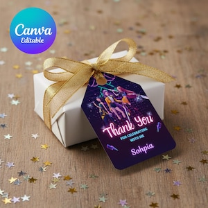 May include: A white gift box tied with a gold ribbon, featuring a custom tag. The tag displays a neon "Thank You" message and a graphic of stylized figures. The background is a wooden surface scattered with star-shaped confetti.