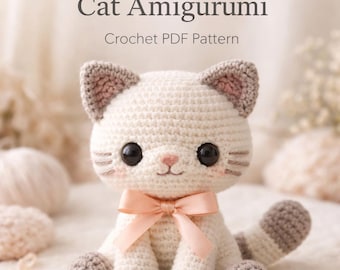 May include: A crocheted cat amigurumi with a cream-colored body, gray ears, paws, and tail. The cat has large black eyes, pink cheeks, and a pink bow. The text "Cat Amigurumi Crochet PDF Pattern" is at the top.