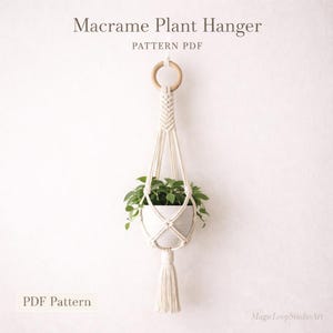 Op de afbeelding: Crèmekleurige macramé plantenhangers met een houten ring en kwast. De plantenhouder bevat een witte keramische pot gevuld met groene planten. Tekst op de afbeelding luidt "Macrame Plant Hanger PATTERN PDF" en "PDF Pattern".