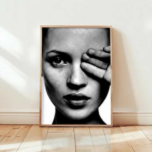 Può includere: Ritratto in bianco e nero di una donna con la mano che copre un occhio. L'immagine è un primo piano del viso, con un focus sull'occhio, il naso e le labbra. Il ritratto è incorniciato in legno.