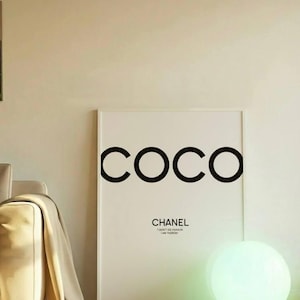May include: A framed white art print with the word "COCO" in large black letters. Below, the text reads "CHANEL" and "I AM FASHION". A glowing orb lamp sits on the floor, casting a green light.