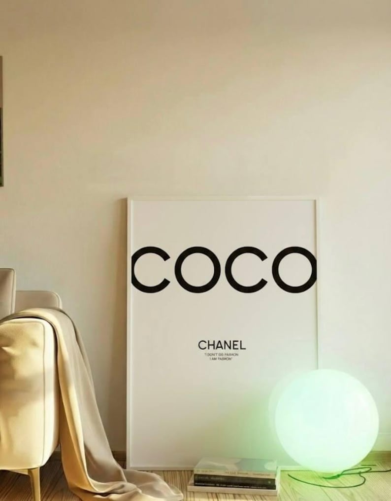 May include: A framed white art print with the word "COCO" in large black letters. Below, the text reads "CHANEL" and "I AM FASHION". A glowing orb lamp sits on the floor, casting a green light.