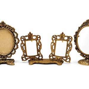 May include: Four antique gold-colored picture frames and mirrors. The frames have ornate, detailed designs. Two are rectangular, one is oval, and one is round. They are displayed on a white background.