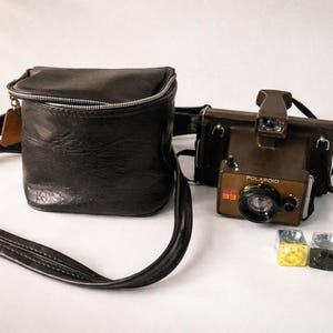 May include: A vintage Polaroid camera with a brown and black leather case and strap. The camera is brown with the word "Polaroid" printed on the front. Also included are four small, colorful shot glasses.