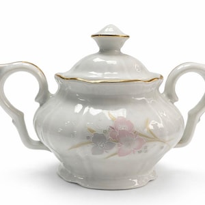 May include: White ceramic sugar bowl with lid, featuring two handles and a floral design in pink and gray. The rim and finial are accented with gold trim. A classic piece for serving sugar.