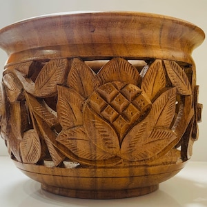 Peut inclure: Un bol en bois sculpté à la main avec des motifs floraux détaillés. Le bol est de couleur marron chaud et présente un motif de fleur de lotus. Le bord et la base sont lisses, contrastant avec les détails sculptés texturés. Ce bol décoratif est adapté à la décoration intérieure.