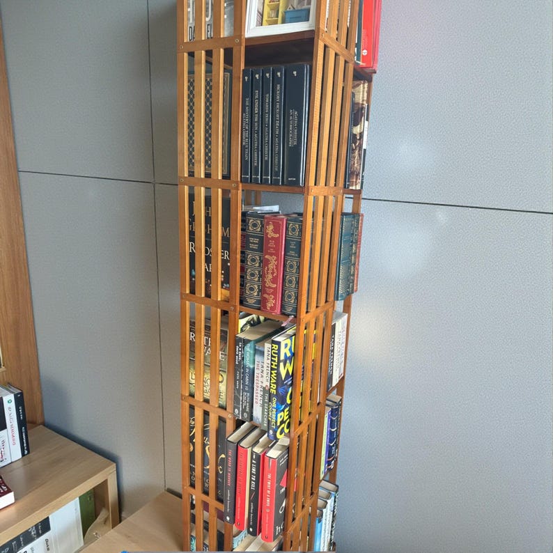 Puede incluir: Una estanter&iacute;a alta de madera clara con dise&ntilde;o de rejilla, llena de libros de varios tama&ntilde;os y colores. La estanter&iacute;a est&aacute; contra una pared gris. Los lomos de los libros crean una exhibici&oacute;n colorida.