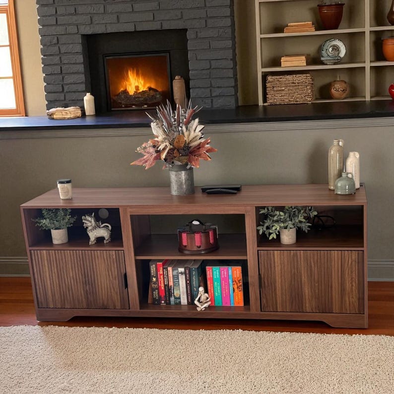 May include: A dark brown wooden entertainment center with two doors, open shelves, and a center compartment. The doors have vertical grooves. The shelves hold books, plants, and decorative items. A fireplace and shelves are in the background.