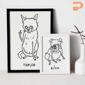May include: Two framed art prints featuring whimsical black and white illustrations of pets. One print shows a cat giving the middle finger, labeled "TAYLOR." The other depicts a dog, labeled "ALICE."