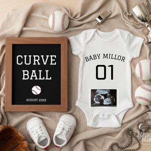 Könnte beinhalten: Baby-Ankündigung im Baseball-Stil. Mit einem weißen Body, Basebällen und einem gerahmten Schild mit der Aufschrift "Curve Ball". Der Body trägt den Aufdruck "Baby Millor" und "01" sowie ein Ultraschallbild.