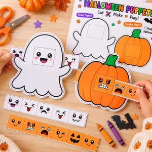 May include: A DIY Halloween puppet craft kit featuring a white ghost and an orange pumpkin cutout. The set includes paper strips with various printed facial expressions, orange scissors, and two crayons. The instruction sheet reads Halloween Puppets.