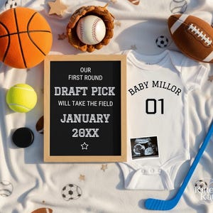 Op de afbeelding: Een witte baby-onesie met de tekst "Baby Millor 01" naast een echografie. Een basketbal, honkbal, voetbal en hockeystick zijn gerangschikt rond een schoolbord met de tekst "Our First Round Draft Pick Will Take The Field January 20XX".