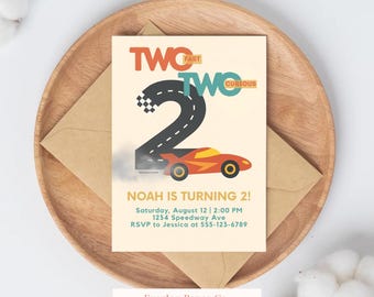 May include: A birthday invitation with a race car theme. The design features the words "TWO FAST TWO CURIOUS" above a large number 2, with a race car and the text "NOAH IS TURNING 2!" The invitation is on a wooden tray with a brown envelope.
