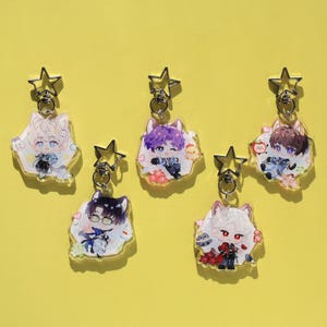 Puede incluir: Cinco llaveros de personajes de estilo anime con cierres en forma de estrella. Cada llavero presenta un diseño de personaje diferente con varios colores de cabello y atuendos. Los llaveros están sobre un fondo amarillo.