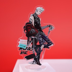 Puede incluir: Un expositor acrílico transparente con un personaje de estilo anime con ropa negra y una chaqueta roja, apoyado en un taburete de bar. El expositor tiene el texto "Darling Yours Bar".