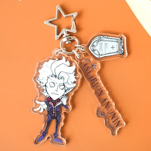 Könnte beinhalten: Ein klarer Acryl-Schlüsselanhänger mit einer Cartoon-Figur mit weißen Haaren, einem lila Outfit und einem Messer. Der Schlüsselanhänger enthält auch einen Grabstein und einen schlüsselförmigen Anhänger mit dem Text "Astarion Ancunin".